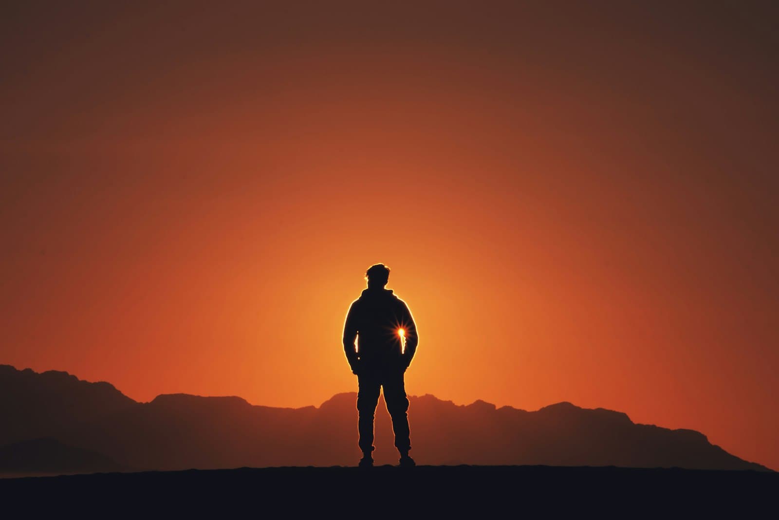 A person standing on a ridge, facing the sunrise